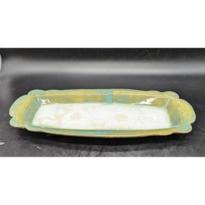 May include: Rectangular ceramic serving tray with a light green and yellow rim and a white interior. The tray features embossed designs of a deer, flowers, and other decorative elements. The tray is ideal for serving food or as a decorative piece.