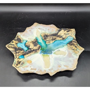 May include: A ceramic plate with an abstract design featuring a white background with blue and green accents. The plate has an irregular, organic shape.