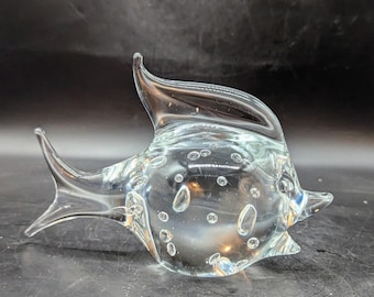 May include: A clear glass sculpture of a fish with air bubbles trapped inside. The fish has a rounded body and a long, thin tail.