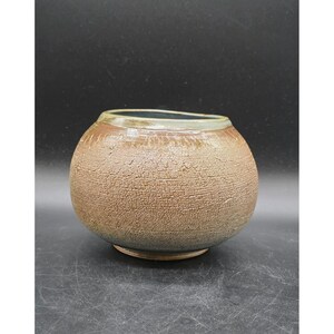 May include: A round ceramic bowl with a textured, cracked surface. The bowl has a brown exterior, a darker brown rim, and a blue-green interior. The pottery has a rustic, earthy aesthetic, suitable for decorative or functional use.