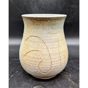 May include: A white ceramic vase with a textured, slightly rough surface. The vase has a wide base and a narrow opening, and it is decorated with a simple, abstract design.