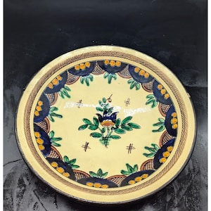 May include: A ceramic plate with a yellow, blue, and green floral design. The plate has a scalloped edge and a brown rim.