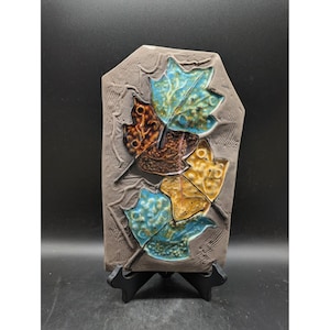 May include: A set of three ceramic mugs with a speckled, cream-colored glaze. Each mug features a different hand-painted floral design in shades of blue, green, and yellow. The mugs have a simple, rounded shape and a comfortable handle.