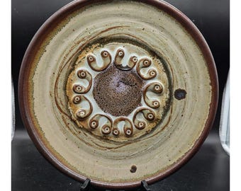 May include: A ceramic plate with a brown and white glaze. The center of the plate has a raised design of white ovals.