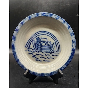 May include: A blue and white ceramic plate with a blue and white design of a boat with a rainbow above it. The plate has a scalloped edge.