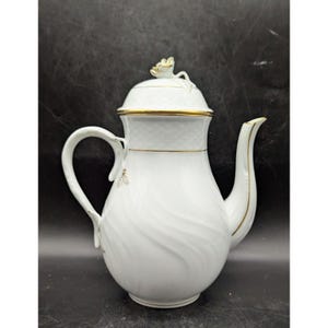May include: White porcelain coffee pot with a lid and a curved handle. The pot features gold trim and a decorative bee design. The lid is topped with a gold floral accent. The pot has a capacity of approximately 40 ounces.