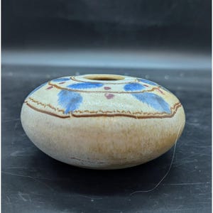May include: A small, round, ceramic vase with a white glaze and blue and red painted designs. The vase has a wide opening at the top.