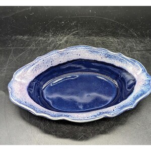 Może przedstawiać: Owalny ceramiczny talerz z falistym brzegiem. Talerz ma głęboko niebieskie wnętrze i obrzeże z gradientem jasnoniebieskiego i lawendowego. Ten ceramiczny talerz jest prawdopodobnie używany do serwowania potraw lub jako element dekoracyjny.