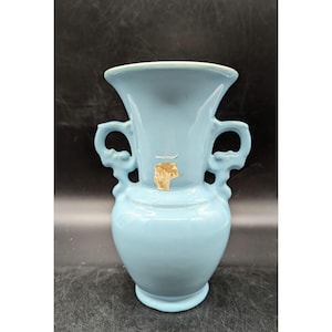 May include: A light blue ceramic vase with two handles. The vase has a classic design and is perfect for displaying flowers.