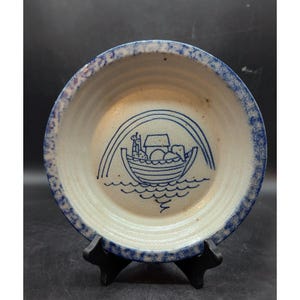 May include: A white ceramic bowl with a blue rim and a blue illustration of Noah's Ark with animals and a rainbow on the inside.