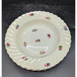 May include: A white ceramic soup bowl with a scalloped edge and a floral pattern. The bowl is decorated with small pink, yellow, and blue flowers.