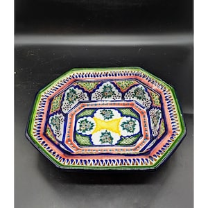 May include: A colorful, octagonal ceramic serving dish with a detailed floral design. The dish features a vibrant palette of green, blue, pink, and yellow, with intricate patterns and a scalloped edge. This decorative piece is ideal for serving food.