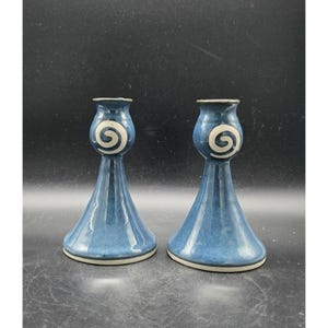 May include: Two blue ceramic candle holders with a white spiral design. The candle holders have a flared base and a narrow top. The rims are white. The background is black.