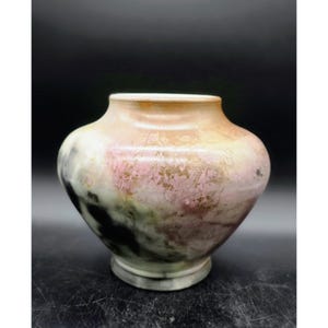 May include: A decorative ceramic vase with a wide body and a narrow neck. The vase features a blend of colors, including pink, beige, black, and green, creating a marbled effect. The base is a lighter shade of gray.