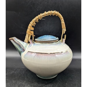 May include: A white ceramic teapot with a blue and brown glaze. The teapot has a woven bamboo handle and a blue lid.