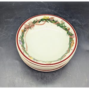 May include: A set of four white ceramic bowls with a red and green Christmas wreath design. The wreath is decorated with ribbons, candy canes, and other festive elements.