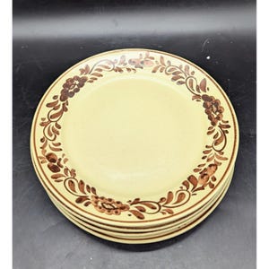 May include: A stack of four ceramic plates with a cream-colored center and a brown floral design around the rim. The plates have a simple, elegant design, suitable for everyday use or special occasions.