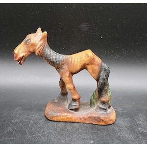 May include: A hand-carved wooden horse figurine. The horse is brown with black mane and tail, and stands on a brown base with green accents. The horse is in a standing position with its head lowered.