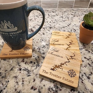Pu&ograve; includere: Quattro sottobicchieri in legno con un design a mappa del lago e il testo "Lake Secession" e "The Trotter Estate".