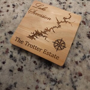 Pu&ograve; includere: Un sottobicchiere in legno con una mappa incisa del lago Secession e il testo "The Trotter Estate".