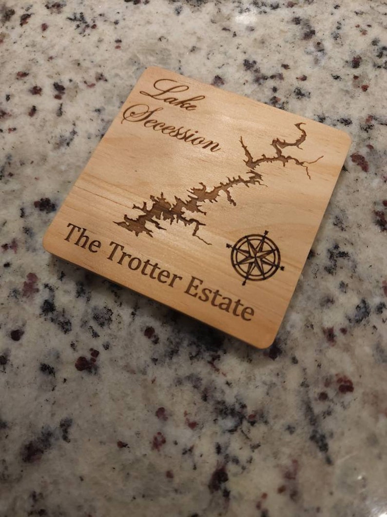 Pu&ograve; includere: Un sottobicchiere in legno con una mappa incisa del lago Secession e il testo "The Trotter Estate".