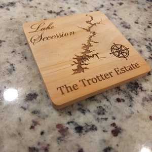 Pu&ograve; includere: Un sottobicchiere in legno con una mappa incisa a laser del lago Secession e il testo "The Trotter Estate".