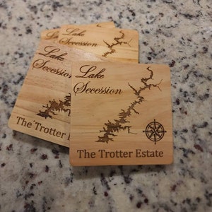 Pu&ograve; includere: Quattro sottobicchieri in legno con un design a mappa del lago e il testo "Lake Secession The Trotter Estate" inciso su di essi. I sottobicchieri presentano un design a rosa dei venti.
