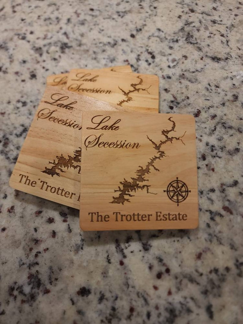 Pu&ograve; includere: Quattro sottobicchieri in legno con un design a mappa del lago e il testo "Lake Secession The Trotter Estate" inciso su di essi. I sottobicchieri presentano un design a rosa dei venti.