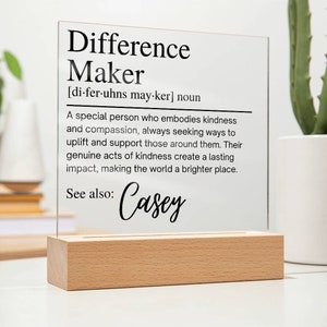 Könnte beinhalten: Eine durchsichtige Acryl-Plakette mit Holzsockel, auf der die Definition von "Difference Maker" und der Name "Casey" stehen.