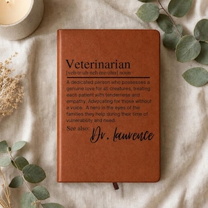May include: A brown leather-like notebook featuring the printed definition of a veterinarian, including the phonetic spelling and the text: "A dedicated person who possesses a genuine love for all creatures... See also: Dr. Laurence" in black ink.
