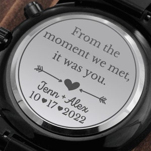 以下が含まれることがあります： 銀色の文字盤と刻まれたメッセージ「From the moment we met, it was you. Jenn + Alex 10.17.2022」が特徴の黒い腕時計