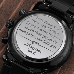 May include: Black wristwatch with a black band and a silver face. The back of the watch has an engraved message that reads: "Dad, thank you for a walk I'll never forget. No matter how much time passes I'll always be your little girl. All my love, Sarah."
