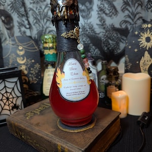 May include: A potion bottle filled with red liquid, labelled "Heart Flare Elixir." The bottle has a dark, textured top and is decorated with a beaded charm. It sits on a vintage book, creating a mystical atmosphere.