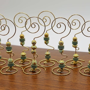 Puede incluir: Conjunto de ocho portafotos de alambre dorado con cuentas verdes y doradas. Cada portafotos tiene un diseño en espiral y una base redonda.