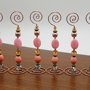 Puede incluir: Seis porta tarjetas de alambre de cobre con cuentas rosadas, melocotón y doradas. Cada porta tarjetas tiene una parte superior en espiral para sujetar una tarjeta.