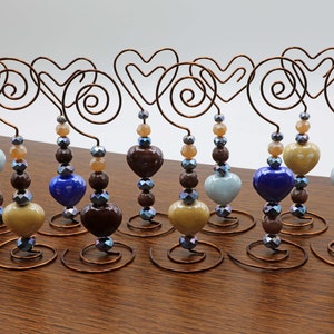 Puede incluir: Diez portafotos de alambre en forma de corazón con cuentas marrones, azules y beige. Cada portafotos tiene una base en espiral.