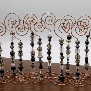 Puede incluir: Un conjunto de 12 soportes para adornos de cuentas negras, plateadas y transparentes. Cada soporte está hecho de alambre de cobre y presenta un diseño en espiral. Los soportes son perfectos para agregar un toque de elegancia a cualquier decoración navideña.