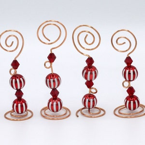 Puede incluir: Seis porta tarjetas de Navidad con forma de adorno de Navidad a rayas rojas y blancas con una base de alambre de cobre y una cuenta de cristal roja.