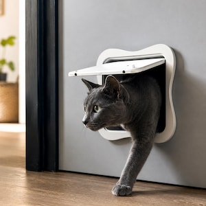 Peut inclure: Un chat gris sortant d'une chatière blanche installée dans une porte grise. Le chat regarde vers la gauche, une patte tendue. La chatière a un cadre incurvé et décoratif et un volet à charnière.