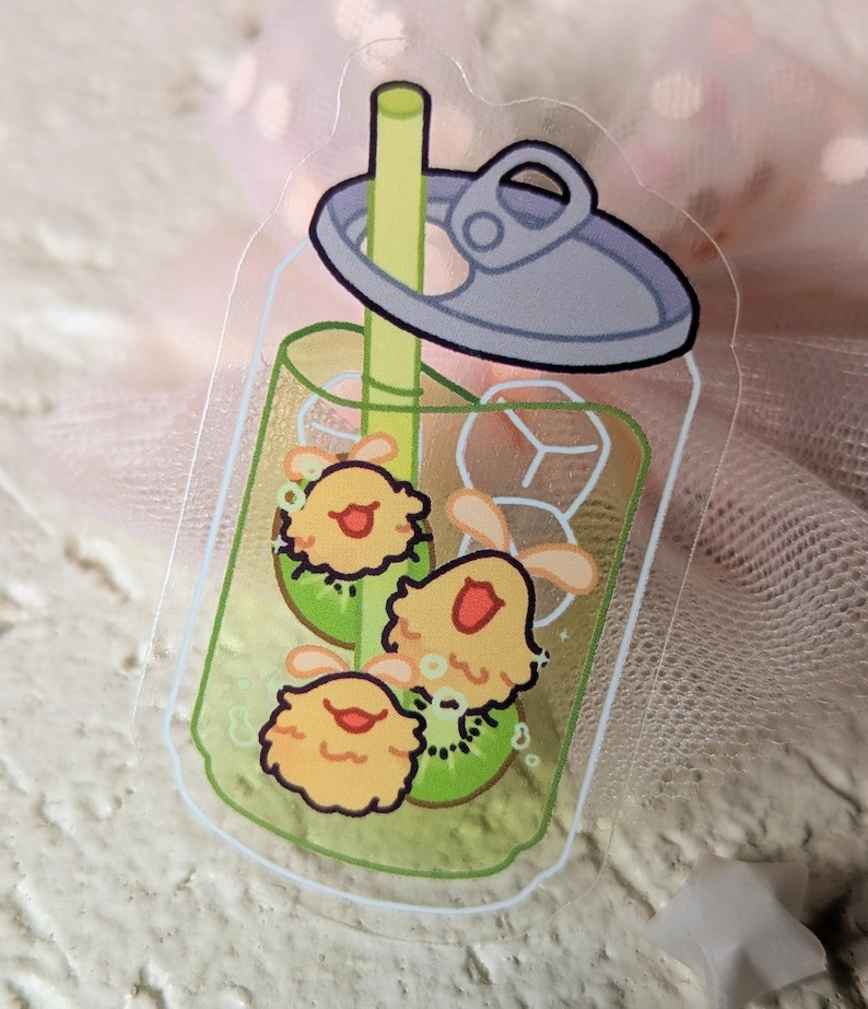 May include: A clear sticker depicting a cartoon drink in a can. The drink is green with kiwi slices and three yellow, smiling characters. The can has a silver lid and a yellow straw.