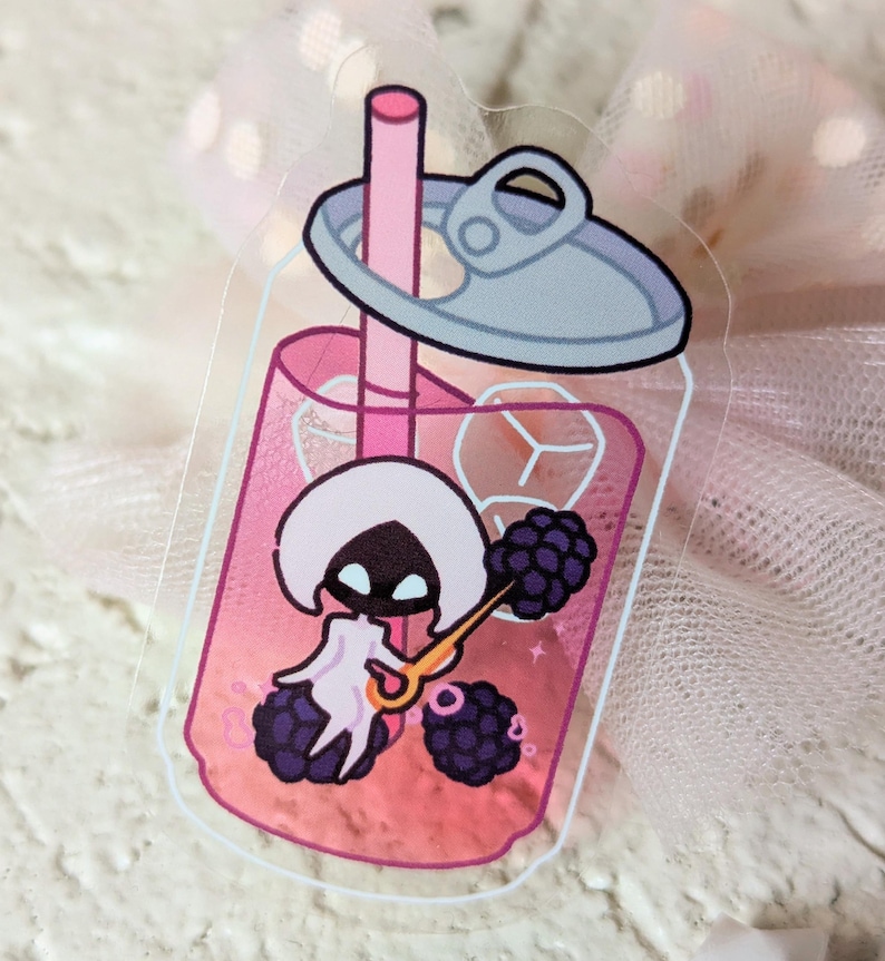 May include: A clear sticker depicting a cartoon character inside a pink drink can with a straw. The character is white with a black face and is holding a golden spoon. Blackberries and ice cubes are also inside the can.