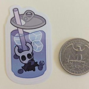 May include: A sticker depicting a cartoon character in a blue drink can with ice cubes and a straw. A quarter dollar coin is next to the sticker.