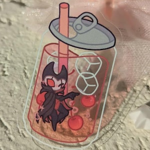 May include: A clear sticker with a cartoon character inside a soda can design. The character is dark with red accents, holding cherries. The can has a pink straw and ice cubes. The design is outlined in white.
