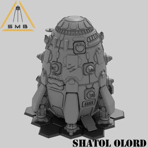 May include: A gray, futuristic spaceship model with detailed panels, rivets, and a domed top. The model has a hexagonal base and the text "SHATOL OLORD" is at the bottom. The logo "SMB" is in the top left corner.