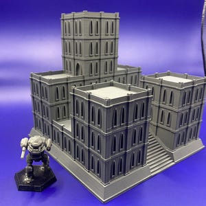 Op de afbeelding: Een grijs 3D-geprint model van een meerverdiepingsgebouw met een gedetailleerde gevel en een trap. Het gebouw heeft meerdere ramen en een plat dak.