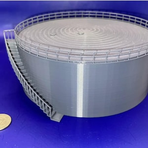 May include: A gray model of a cylindrical storage tank with a spiral top and a railing around the perimeter. A staircase leads up to the top. A coin is next to the tank.