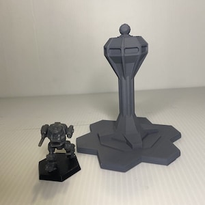 May include: A gray 3D-printed model of a futuristic tower with a hexagonal base and a small robot figure on a black hexagonal base. The tower has a cylindrical stem and a bulbous top.