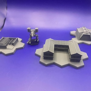 May include: A set of four grey 3D printed miniature buildings and a mech on hexagonal bases. The buildings are a small factory, a two-storey building with a flat roof, a building with a pitched roof, and a building with a curved roof.