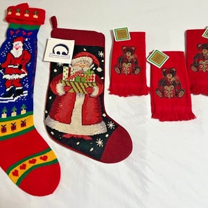 Puede incluir: Tres calcetines de Navidad rojos con diseños bordados. Un calcetín presenta a un Papá Noel patinando sobre hielo, otro presenta a un Papá Noel sosteniendo regalos y el tercero presenta a un oso de peluche sosteniendo un regalo.