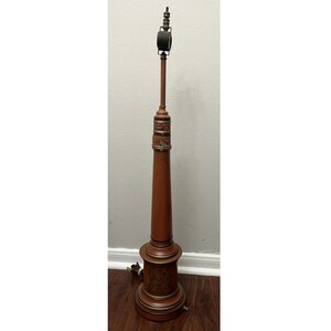 May include: A tall, wooden lamp shaped like a fire hose with a black and silver top. The lamp has a brown base with gold accents and a floral design.